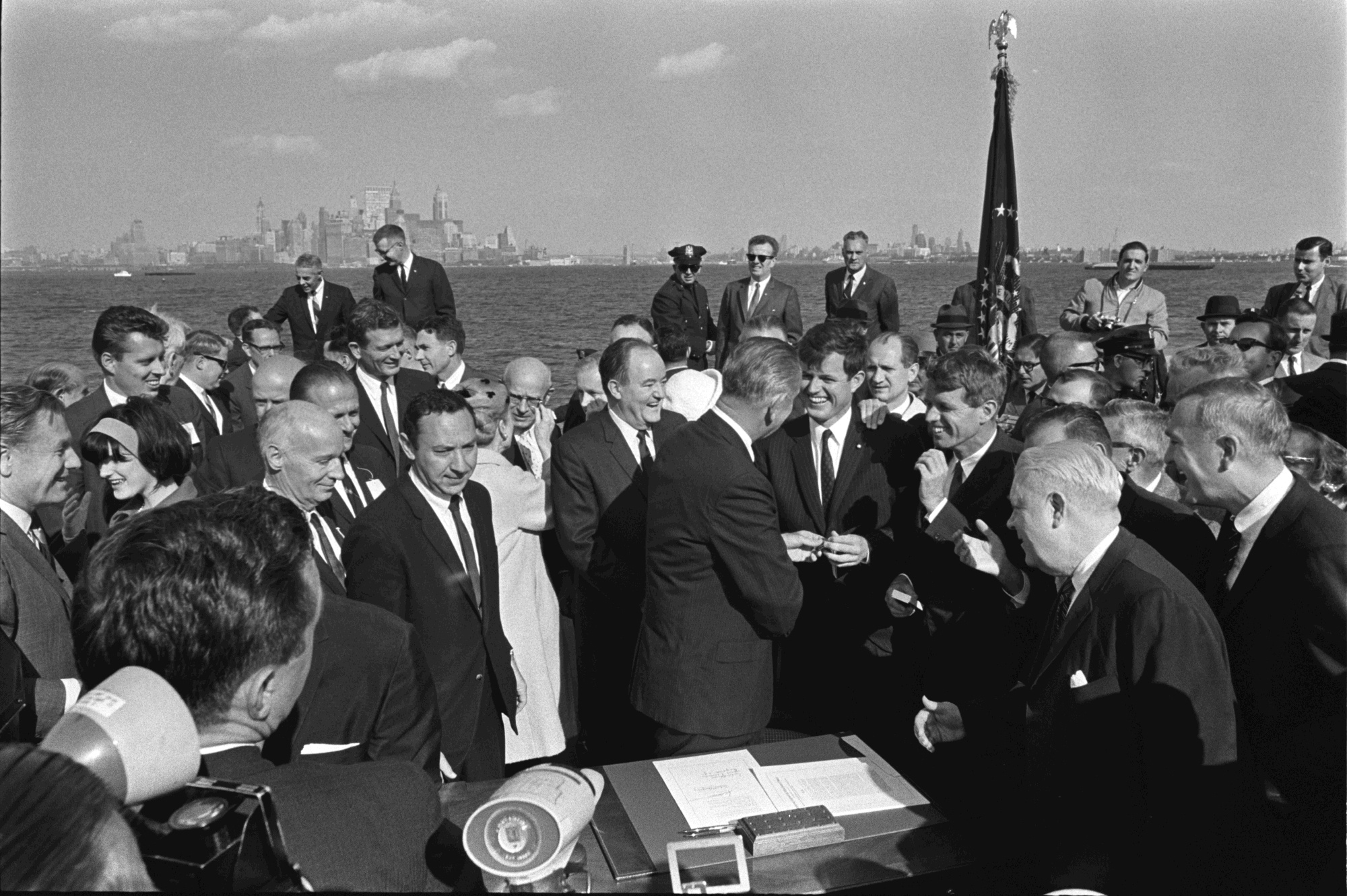 President Lyndon B. Johnson gives Edward (Ted) Kennedy a pen, while others, including Robert Kennedy and Vice President Hubert Humphrey look on.