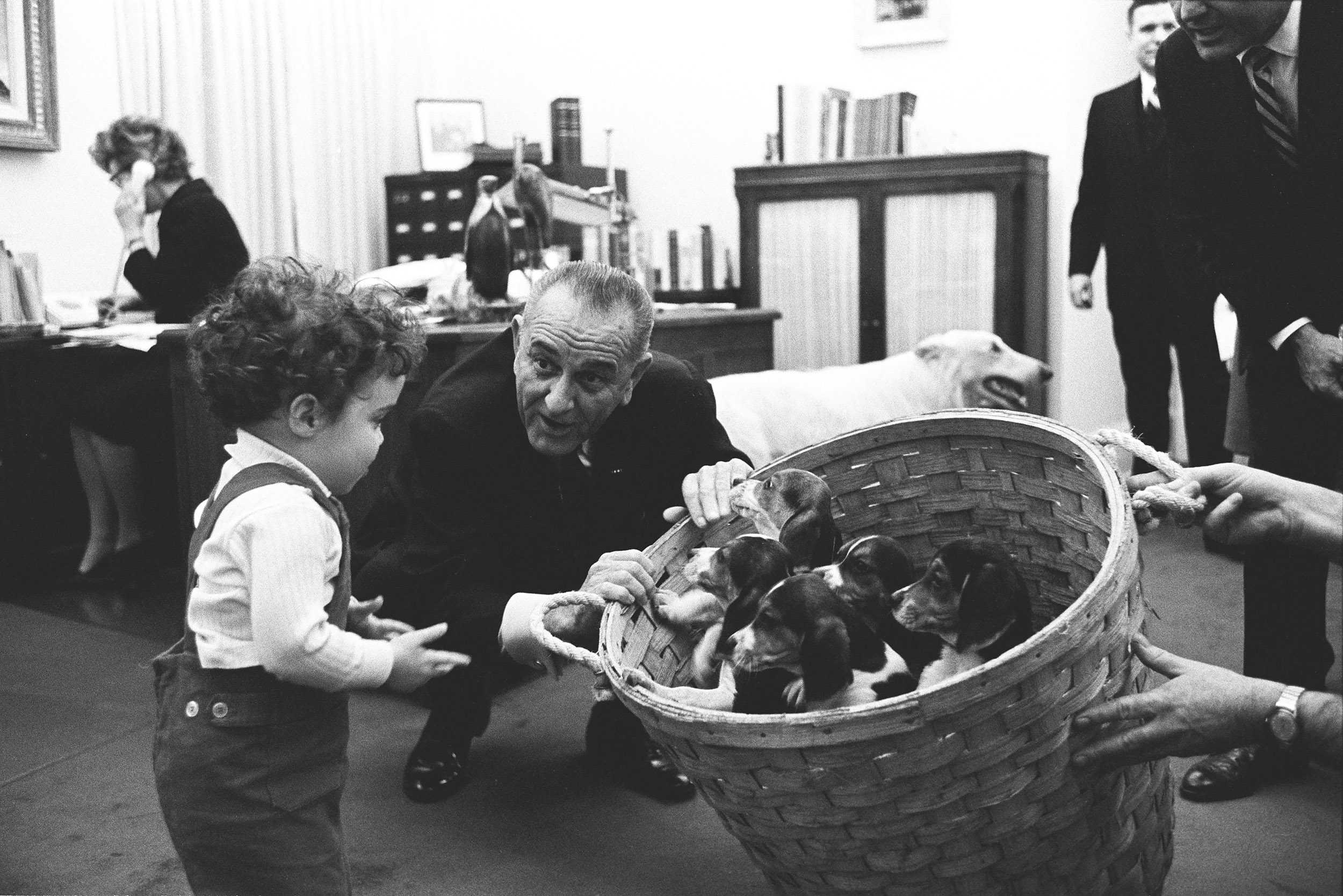 President Johnson shows a basket of Beagle puppies to special assistant Jack Valenti's daughter, Courtenay.