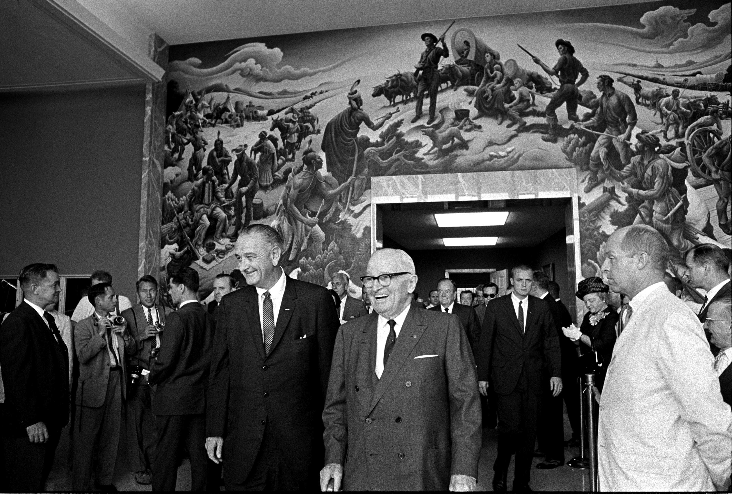President Lyndon B. Johnson, President Harry S.Truman and others walk through the Truman Library. In the background is a mural painted by Thomas Hart Benton "Independence and the Opening of the West". LBJ Library photo by Yoichi Okamoto #A986-26A.