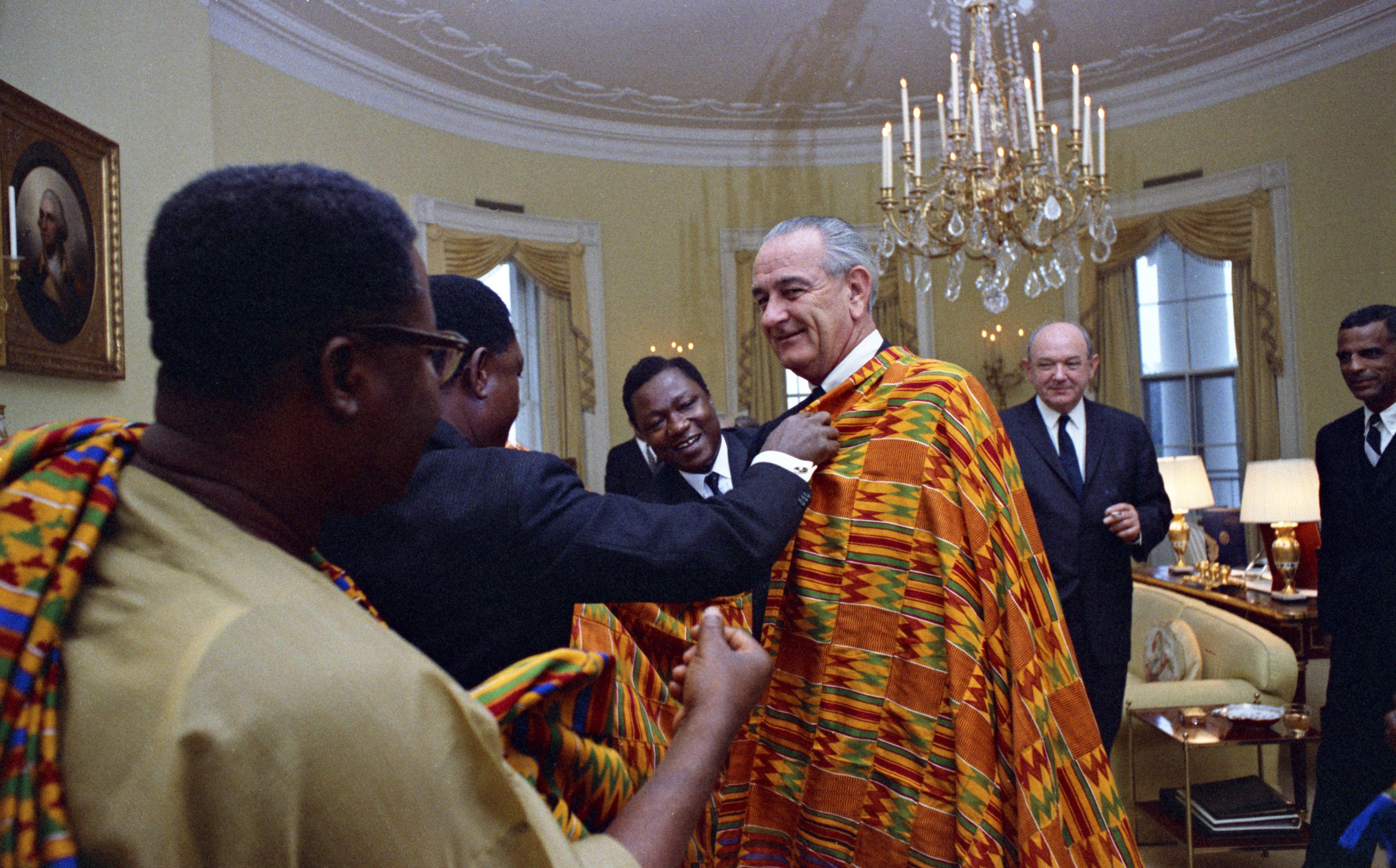 Gen. Joseph A. Ankrah and members of his entourage adorn President Lyndon Baines Johnson with a Kente textile from Ghana as Sec. Dean Rusk and others look on. LBJ Library photo by Yoichi Okamoto #C6901-23.