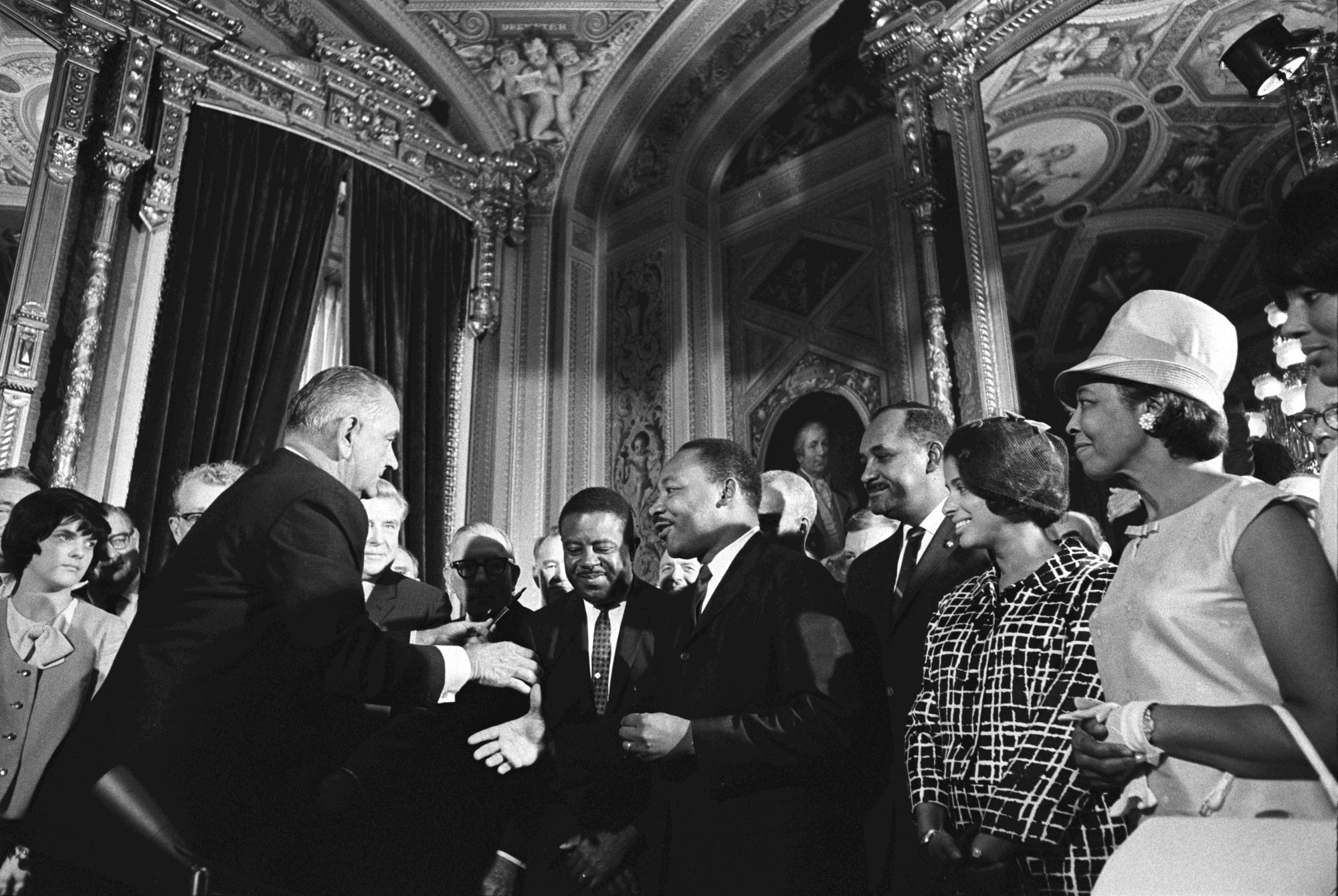 President Lyndon B. Johnson moves to shake hands with Martin Luther King, Jr. while others look on.