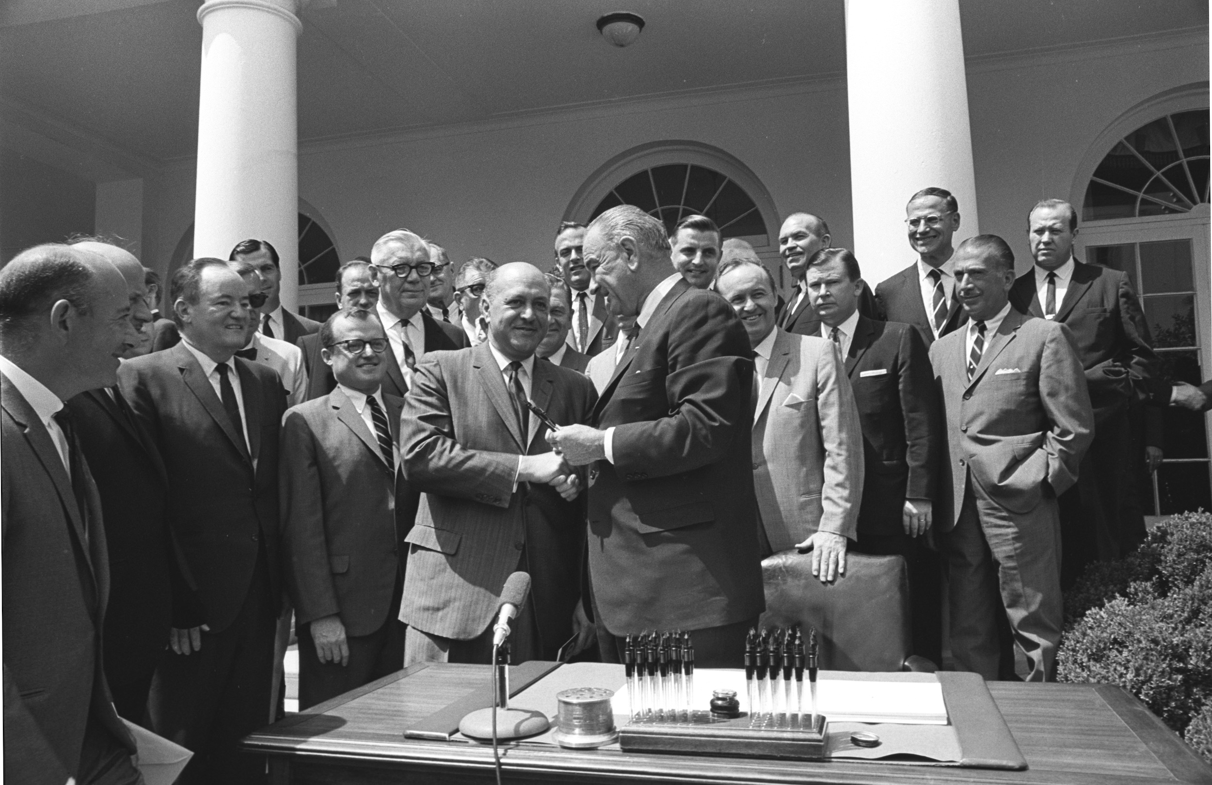 President Lyndon B. Johnson shakes hands with Robert C. Weaver as others look on.