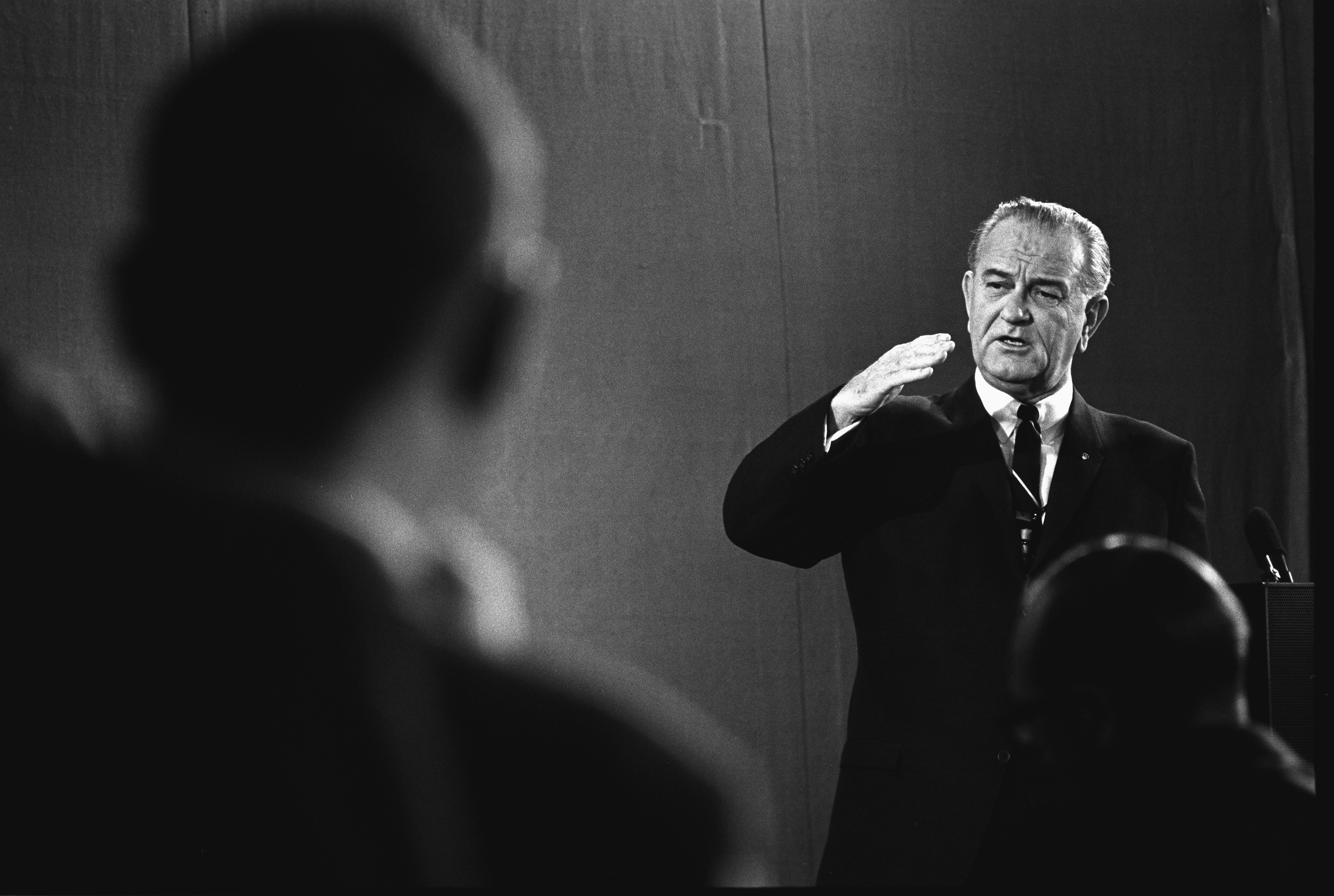 Speaking next to a podium, President Johnson addresses an audience. 