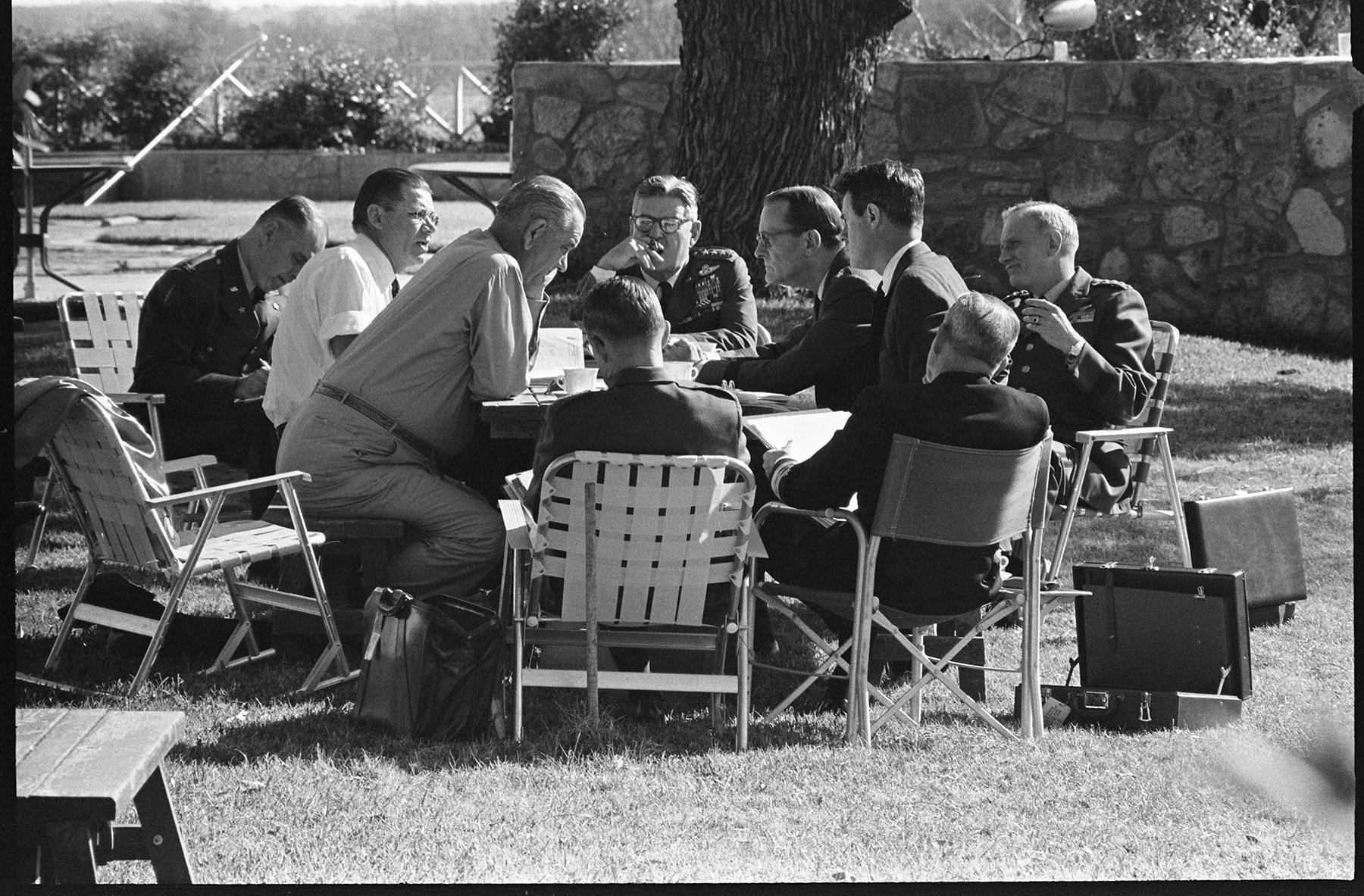 While sitting around a picnic table, President Johnson meets with his Joint Chiefs of Staff on the front lawn of his LBJ ranch home.