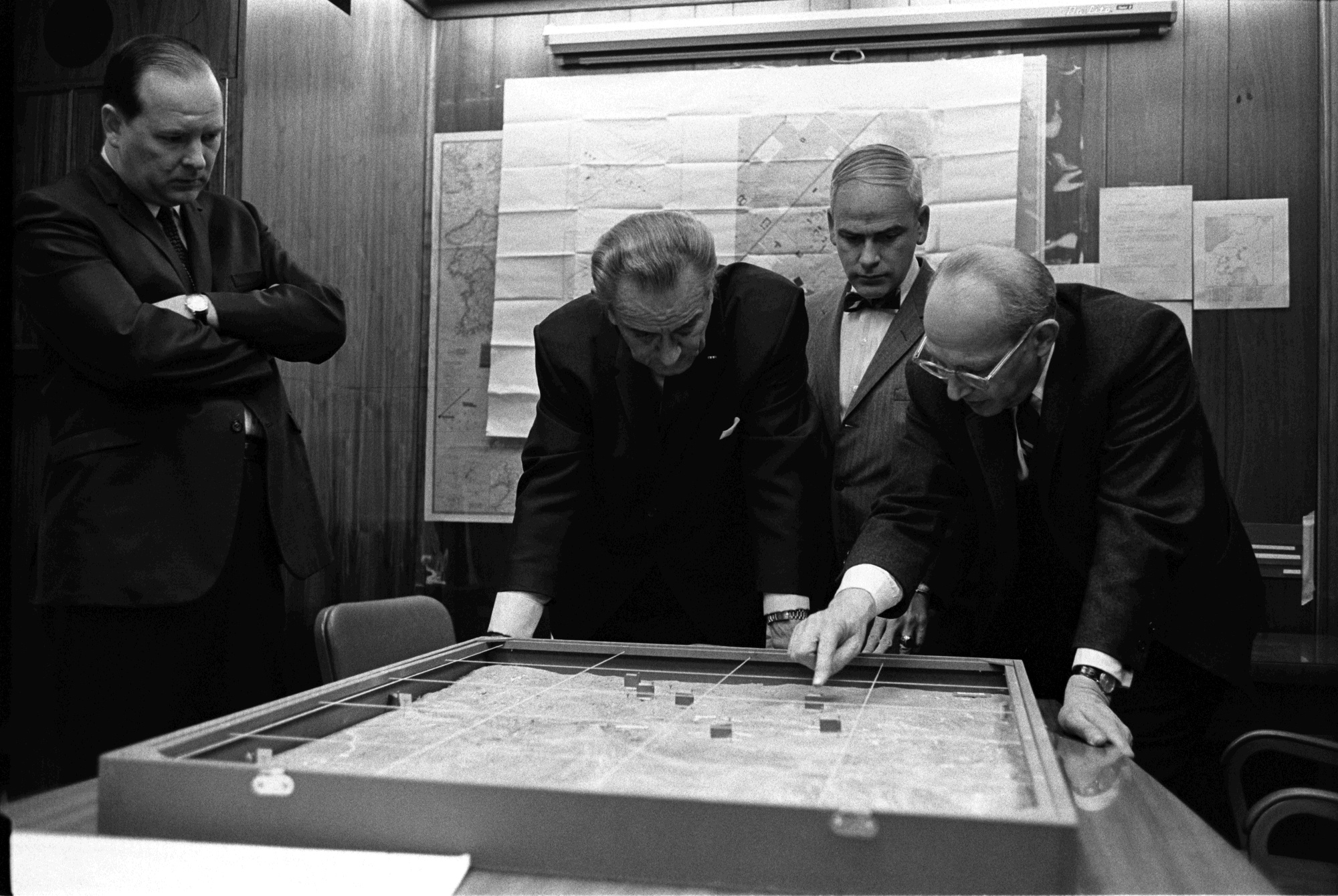 George Christian, President Johnson, Gen. Robert Ginsburg, and Walt Rostow look down at a map on a table in the Situation Room.