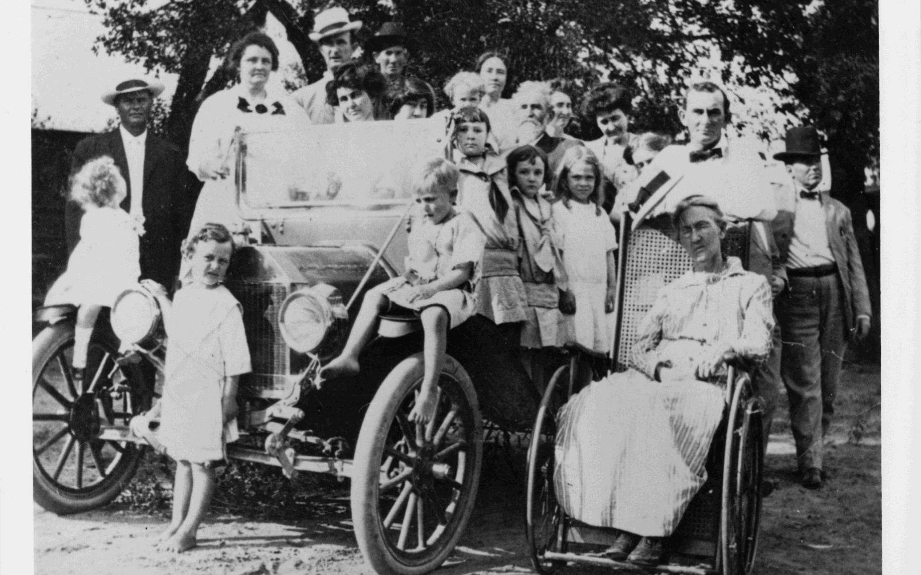 Family gathering: Lyndon B. Johnson (ca. 4 years old) is standing in front of automobile. 3rd adult from left (back row) is Sam Ealy Johnson, Jr. Rebekah Baines Johnson is in front of him. Eliza Bunton Johnson seated in wheelchair.