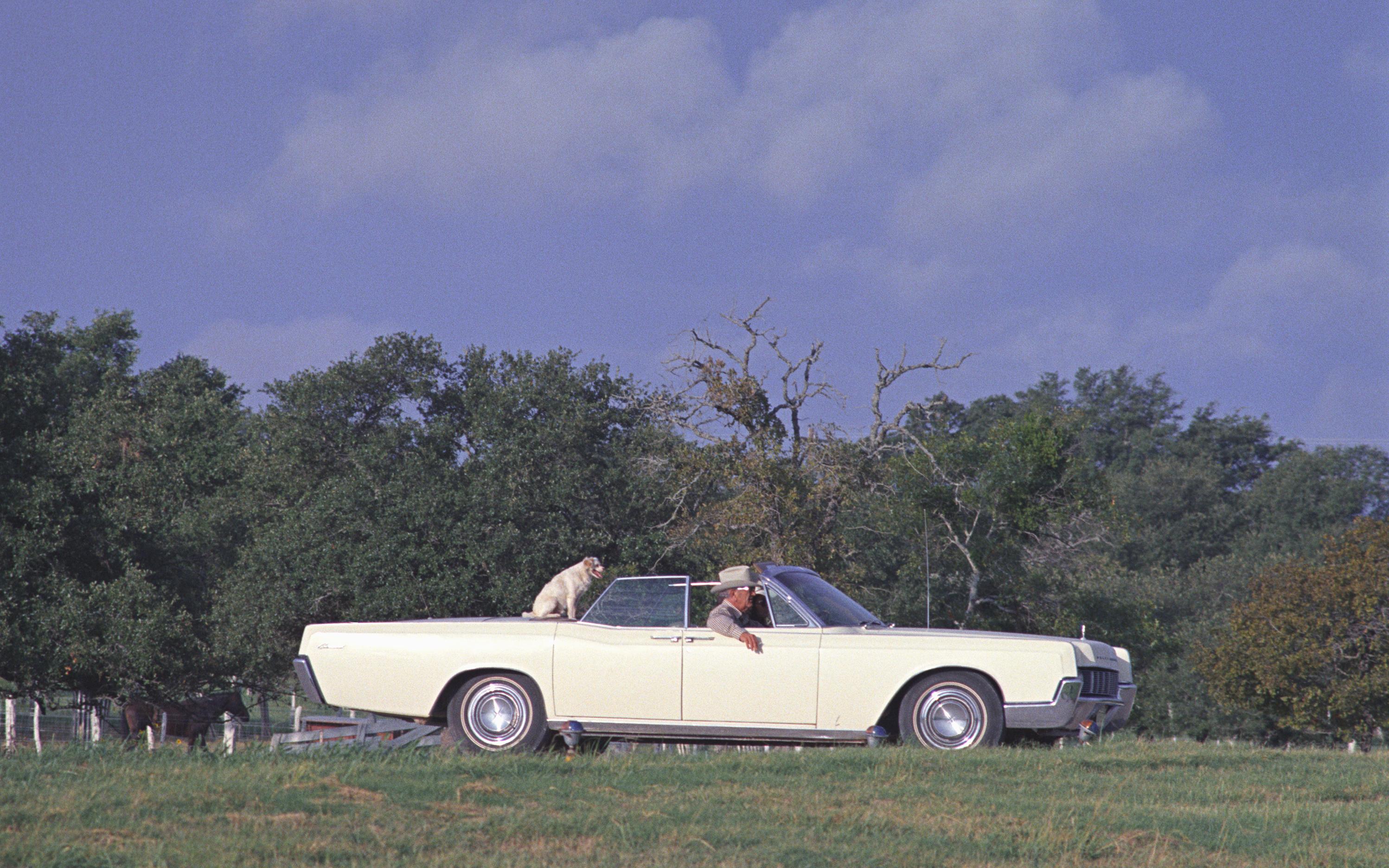 LBJ riding in a Lincoln convertible with his dog, Yuki, sitting in the back.
