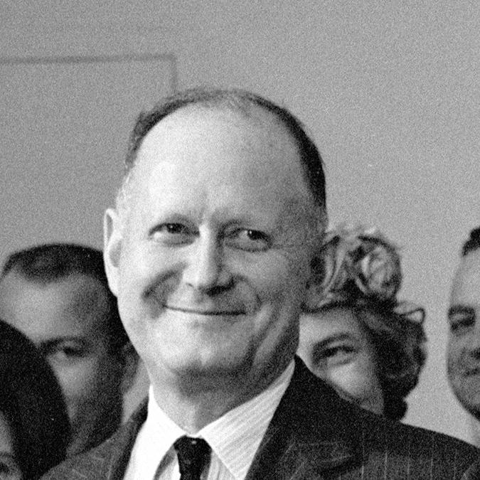 C. Douglas Dillon stands next to President Johnson as the president gives remarks from a podium.