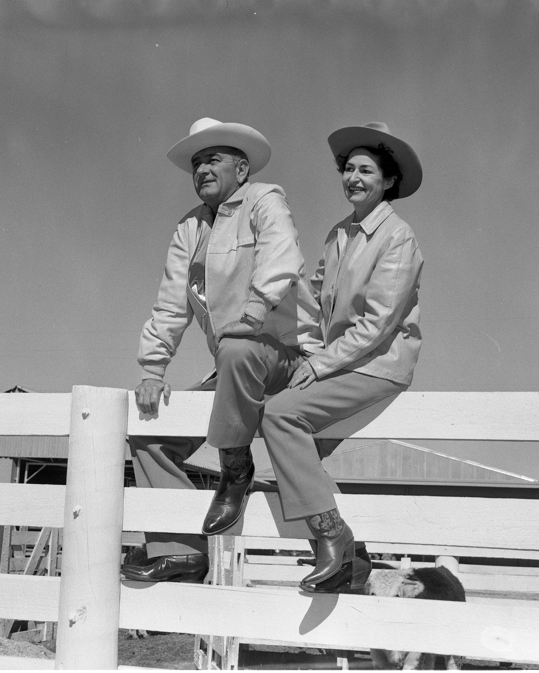 Lyndon B. Johnson and Lady Bird Johnson sit on top of a fence at the LBJ Ranch.