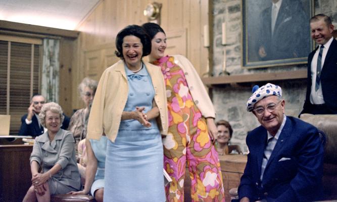 President Johnson wears a blue, polka dotted hat, given to him as a birthday present, as Lady Bird Johnson and daughter Lynda laugh. [LBJ Library photo by Kevin Smith, C2944-16. Aug. 27, 1966.]