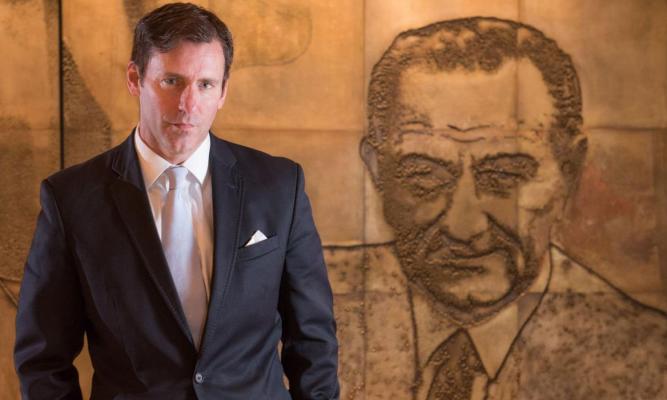 Mark K. Updegrove stands in front of a mural, featuring President Johnson, at the LBJ Presidential Library.